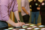 Person writing on a We Connect Name Tag at a table with other people in the background