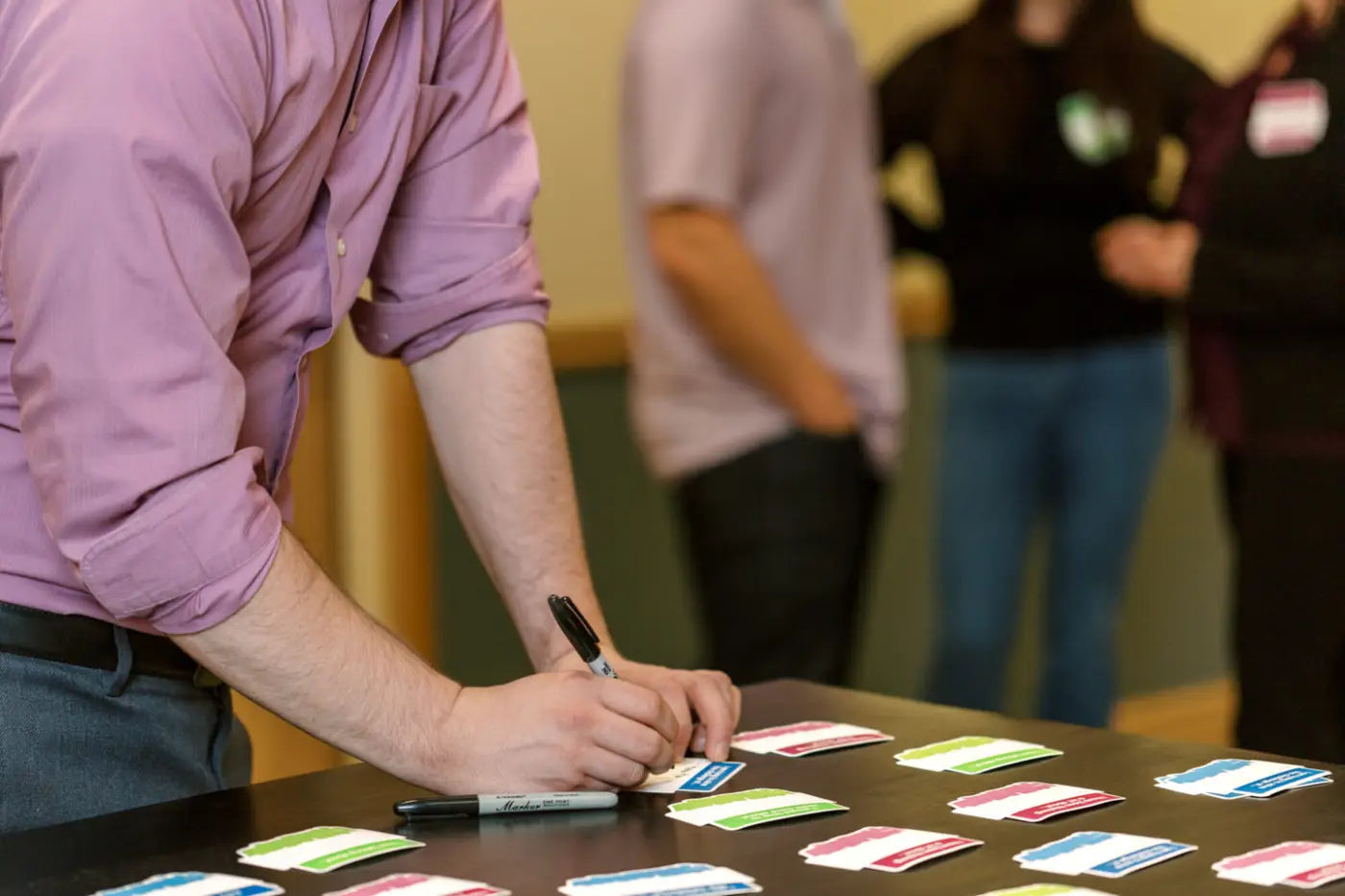 Person writing on a We Connect Name Tag at a table with other people in the background