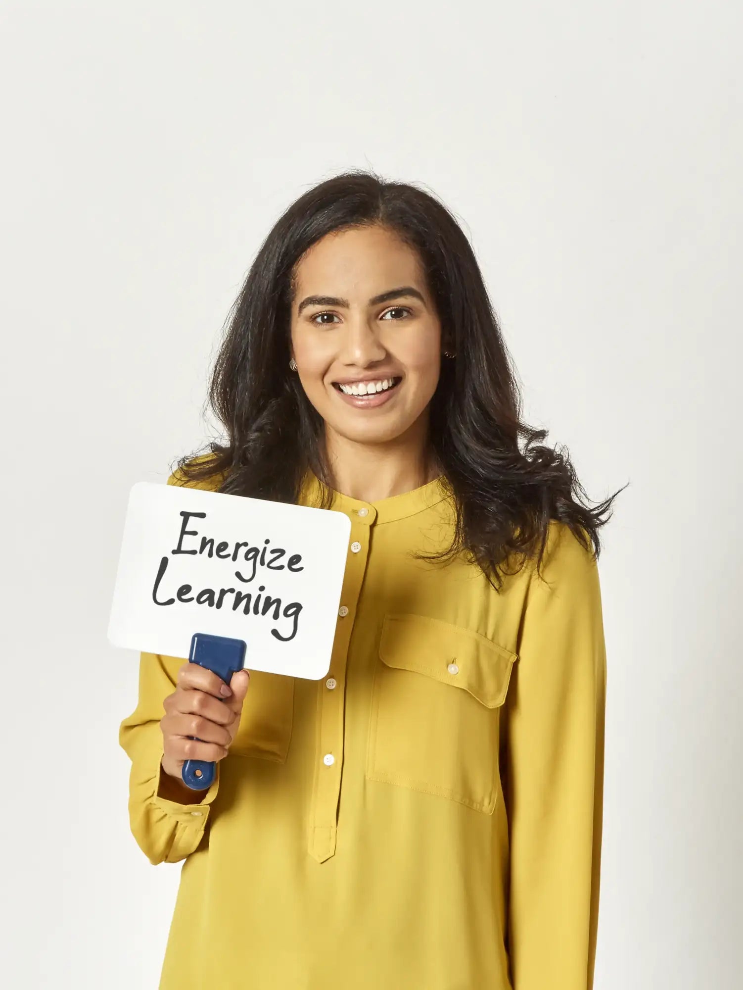 A woman in a mustard-yellow button-up shirt holds a white rectangular sign with the words ’energize learning’ written on it.